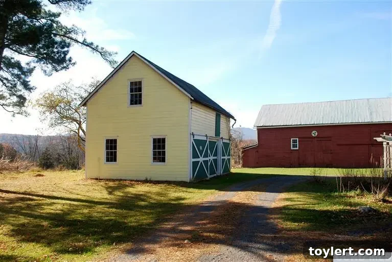 The charming exterior of a classic Upstate New York farmhouse with a vibrant red barn in the background, surrounded by lush green land.