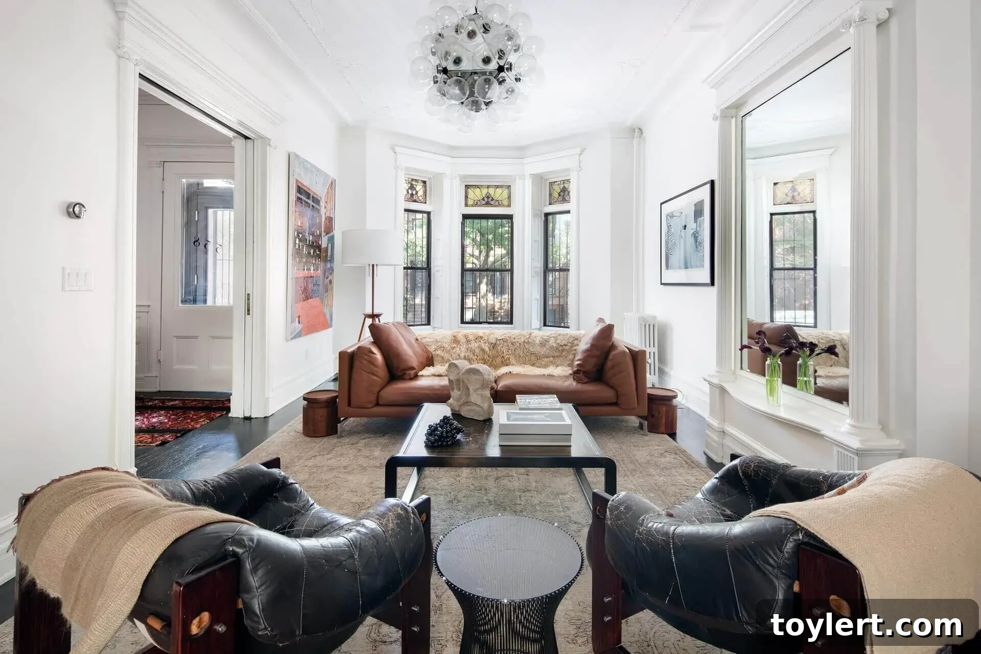 Interior of a renovated historic brownstone in Bed Stuy, featuring white painted woodwork, original moldings, a grand pier mirror, and elegant fireplaces.
